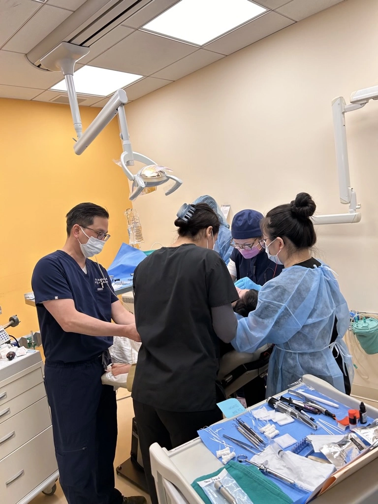 Dr. Marn performing a dental procedure with a surgical team in a well-equipped clinical setting.