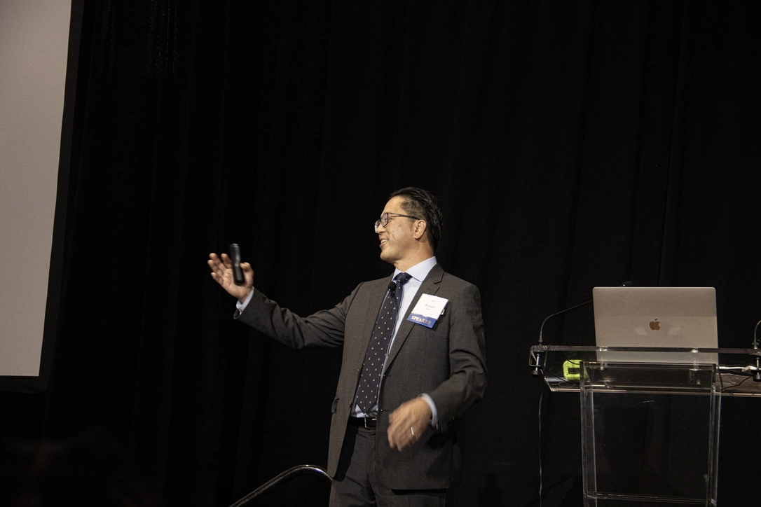 Dr. Marn giving a presentation on stage at a professional conference, holding a remote clicker.