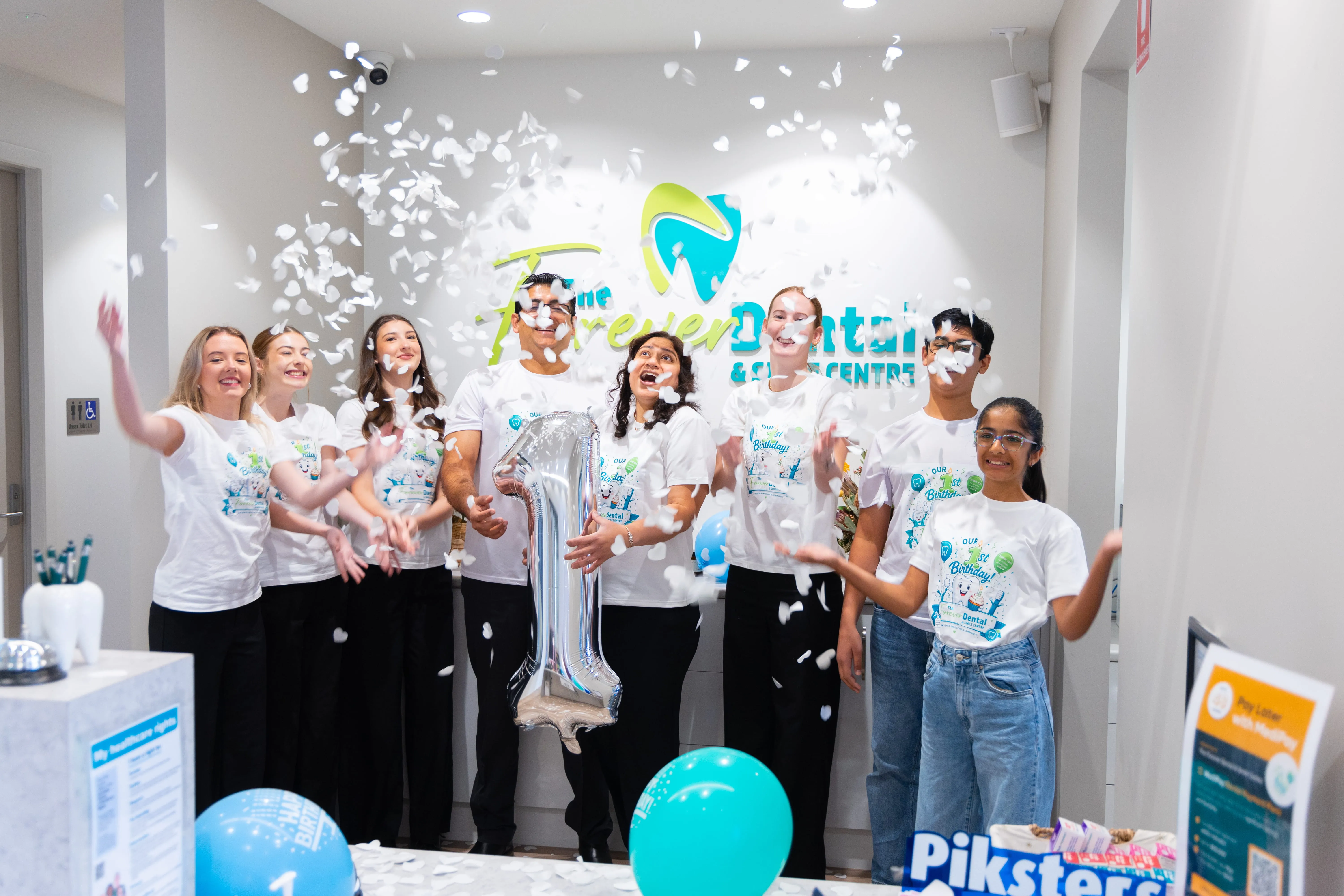 Forever Dental & Smile Centre team celebrating their first anniversary with confetti in the clinic reception.