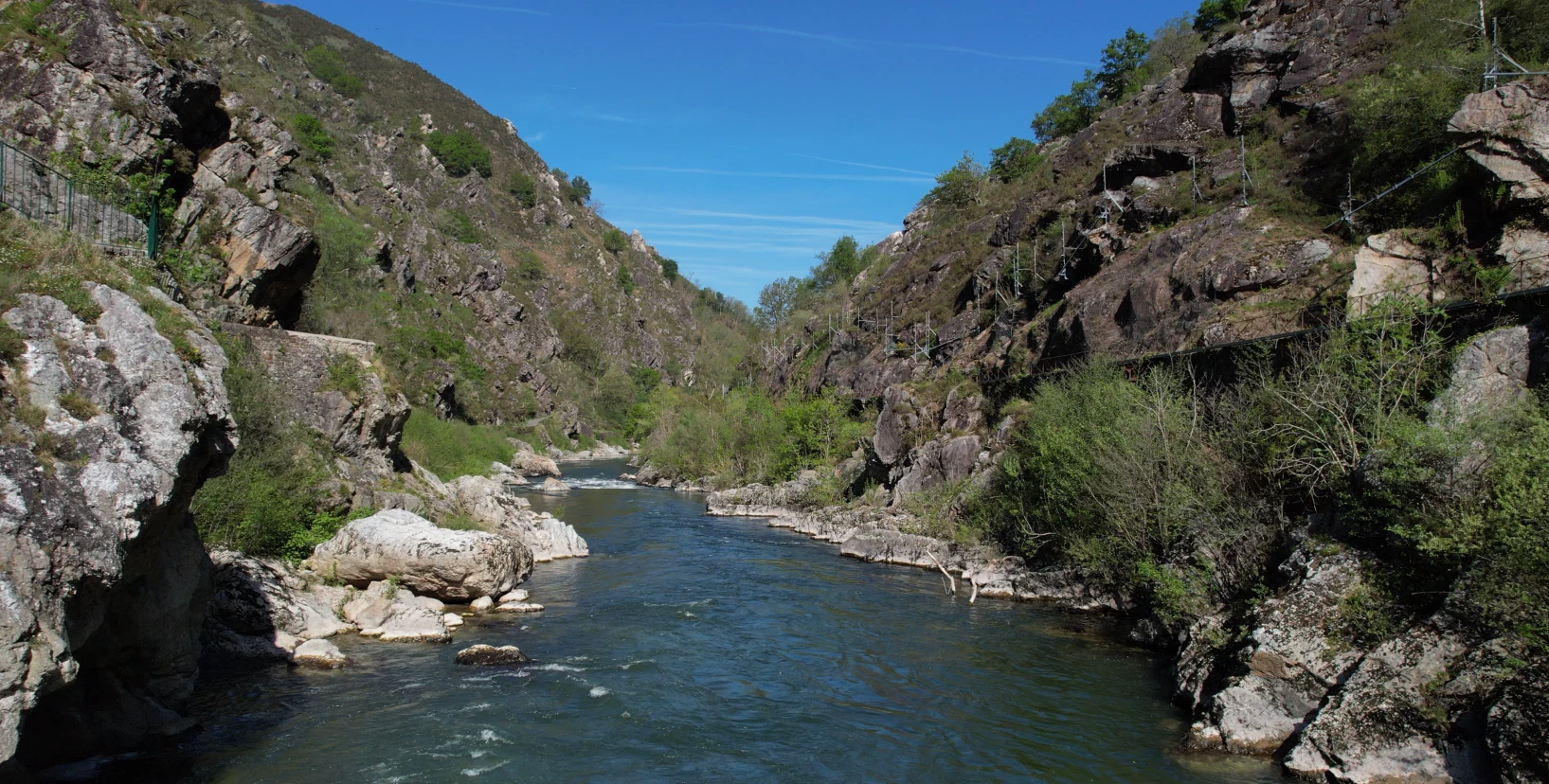Pas de Roland - Rivière coulant entre des falaises rocheuses couvertes de végétation sous un ciel bleu clair.
Séjours à vélo clé en main de The Family Bike.