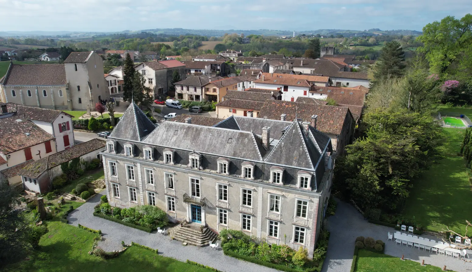 Vue aérienne d'un grand manoir historique avec un toit en ardoise, entouré de jardins bien entretenus et de village aux toits de tuiles.
Hébergement proposé dans les séjours à vélo clé en main de The Family Bike.