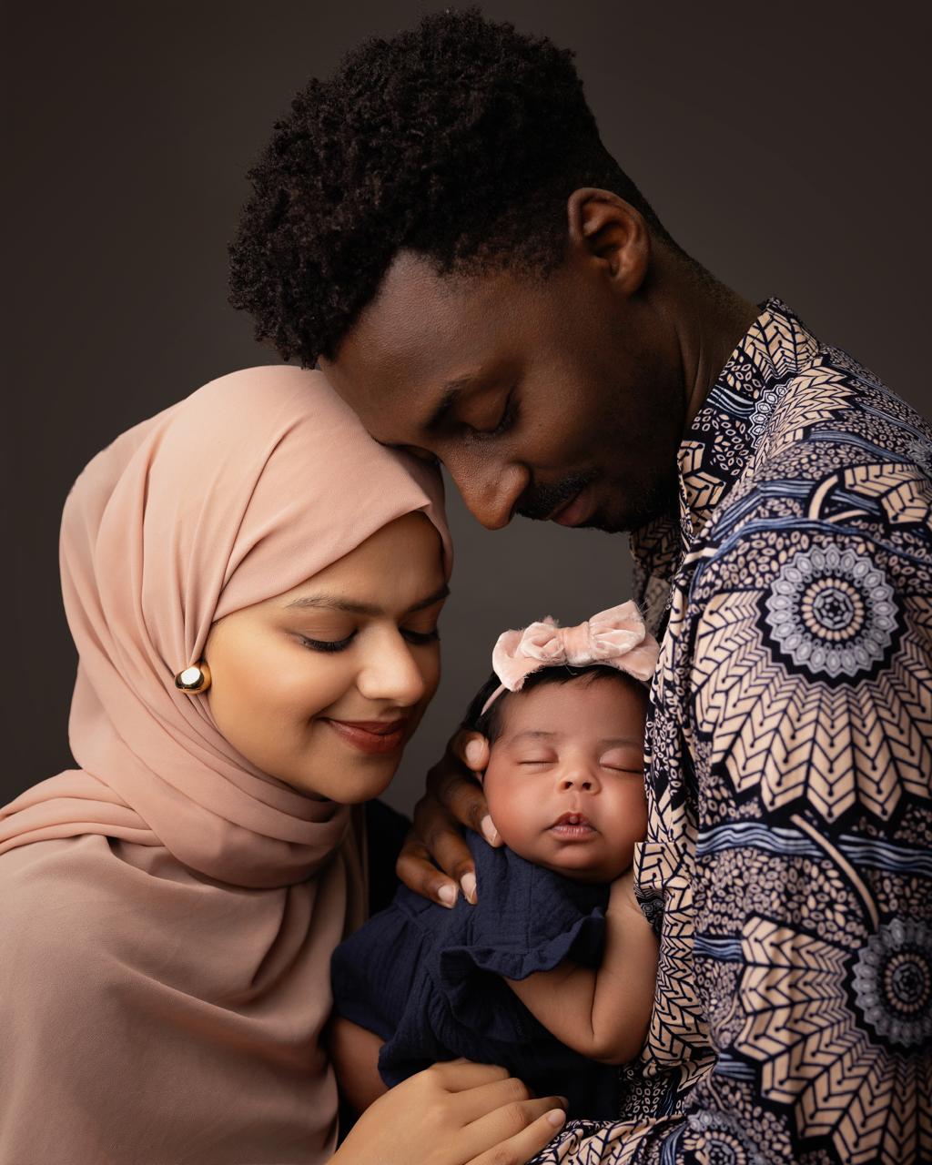 Loving couple holding their sleeping baby girl dressed in navy with a pink bow on her head.