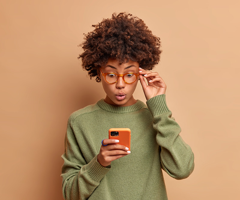 Verraste vrouw met krullend haar houdt smartphone vast