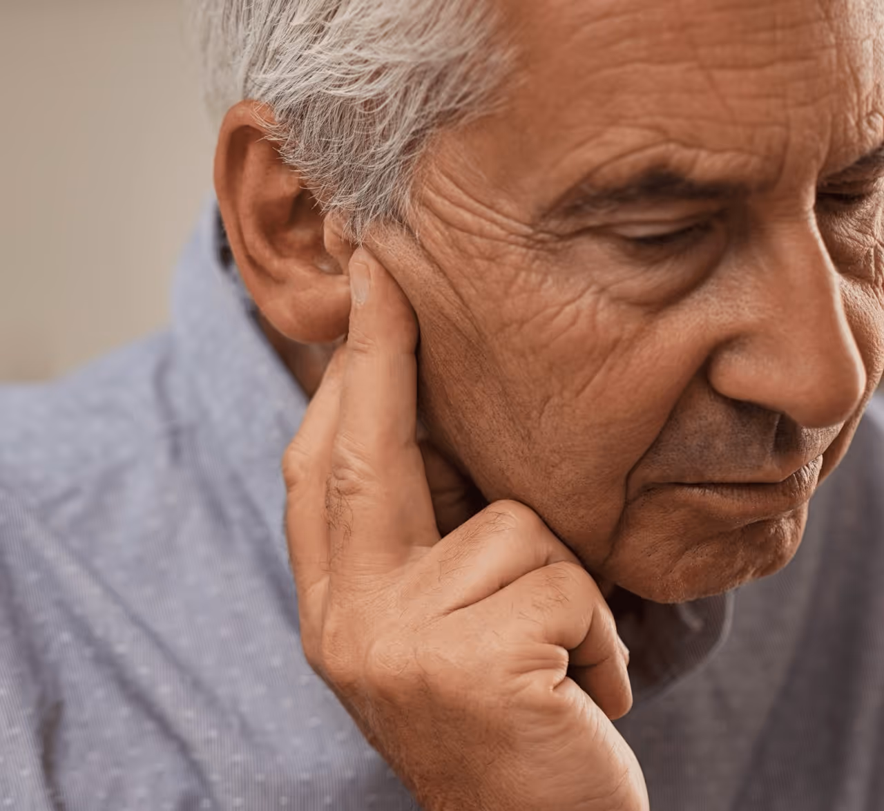 Oudere man met gehoorproblemen houdt hand bij oor tijdens audiologisch onderzoek