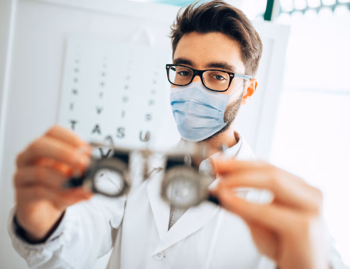 Optometrist houdt een meetbril vast met een mondkapje op. 