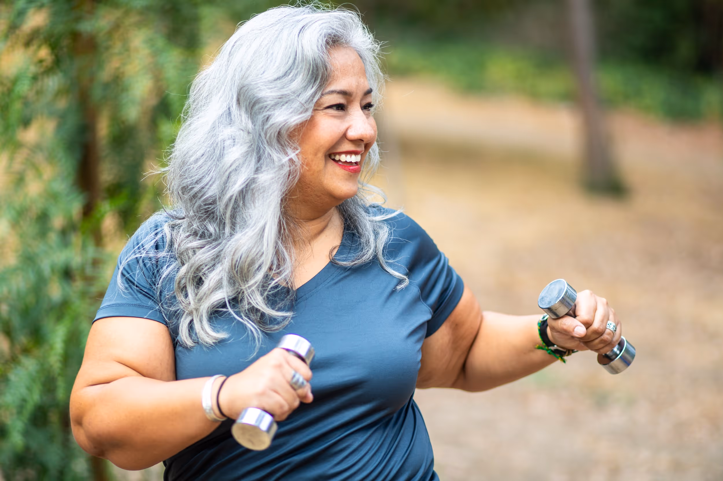 Een vrouw sport met  dumbels in haar beide handen in de een park. 