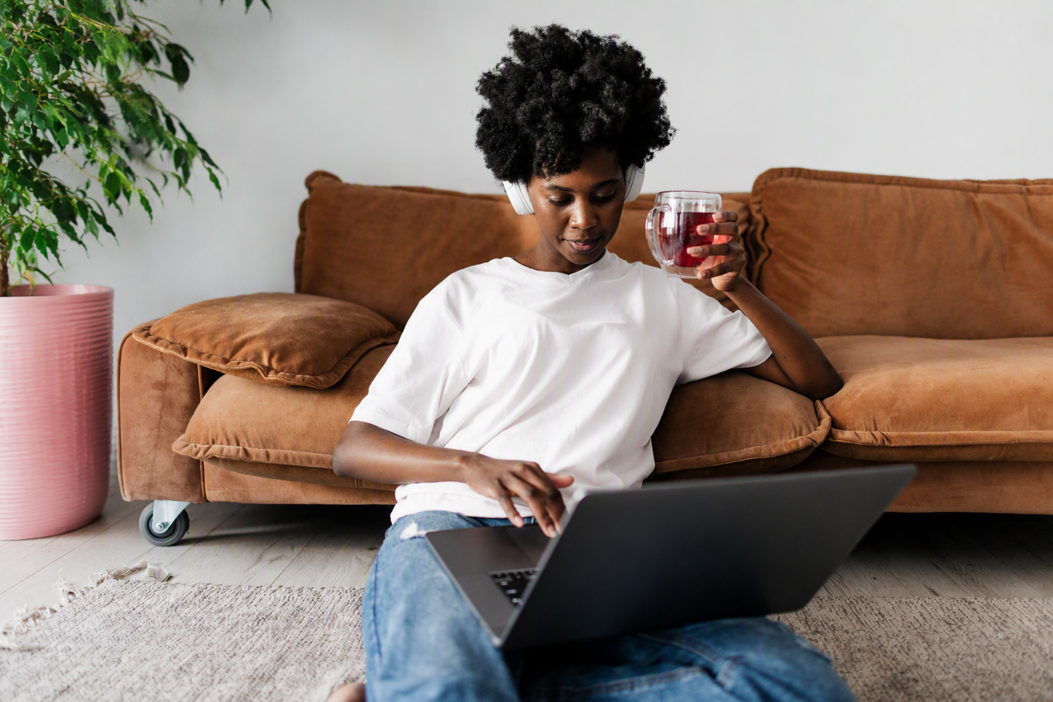Vrouw zit voor de bank met een kop thee bezig op de laptop