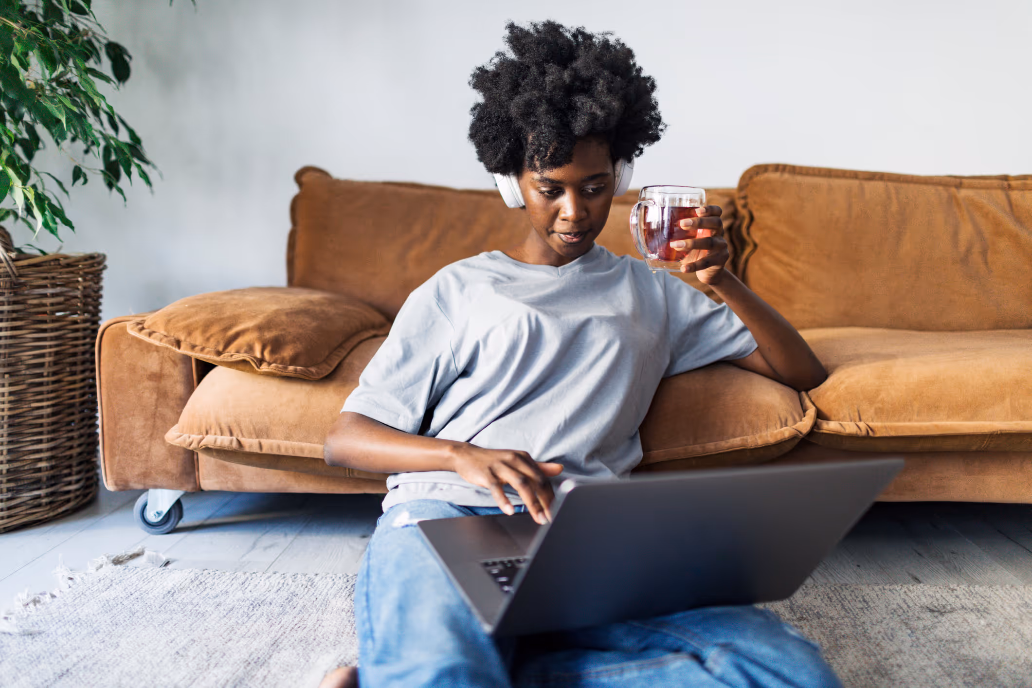 Vrouw zit voor de bank met een kop thee bezig op de laptop 