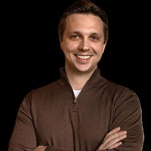 Portrait of smiling man in brown pullover, arms crossed

