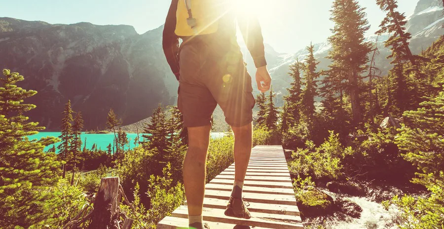 A man hiking across a wooden bridge surrounded by scenic nature, symbolizing the journey to better health and vitality that Gameday Men's Health supports