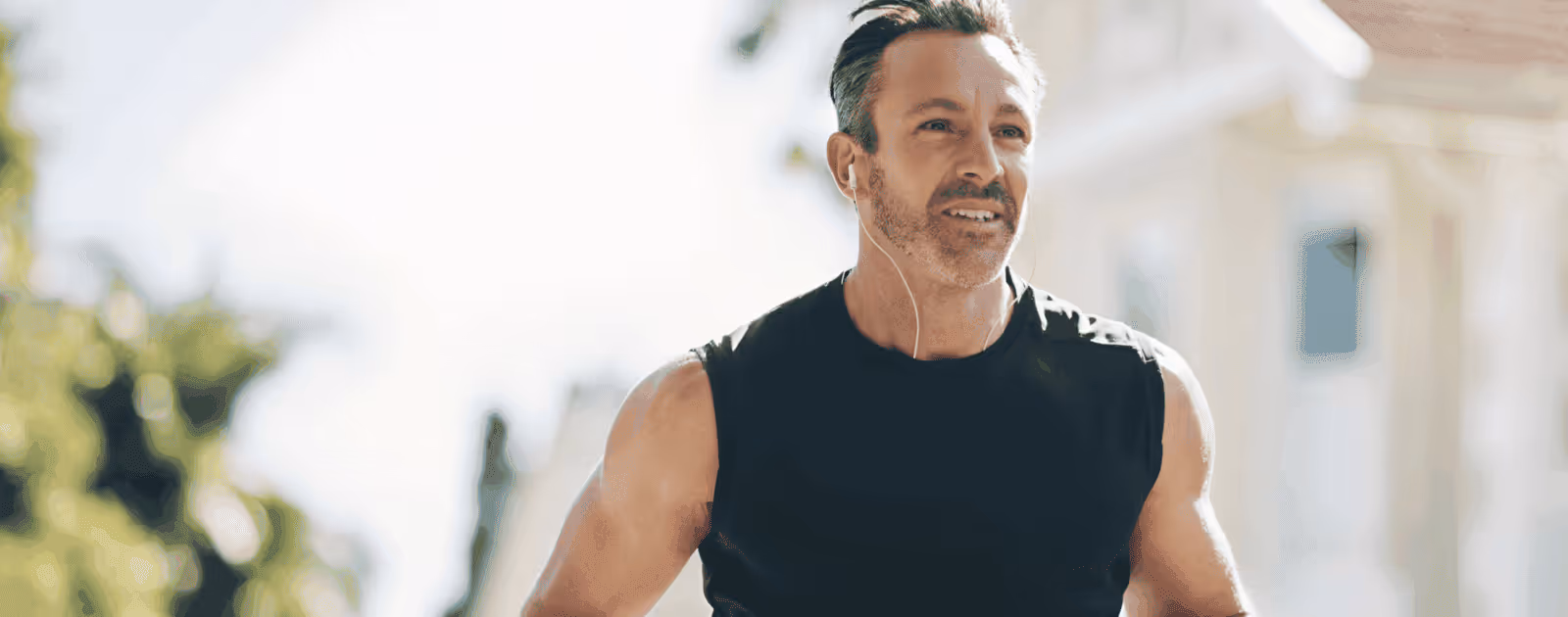 Middle-aged man jogging outdoors with earbuds in, representing the energy, endurance, and recovery benefits of Tri Amino Acids for men.