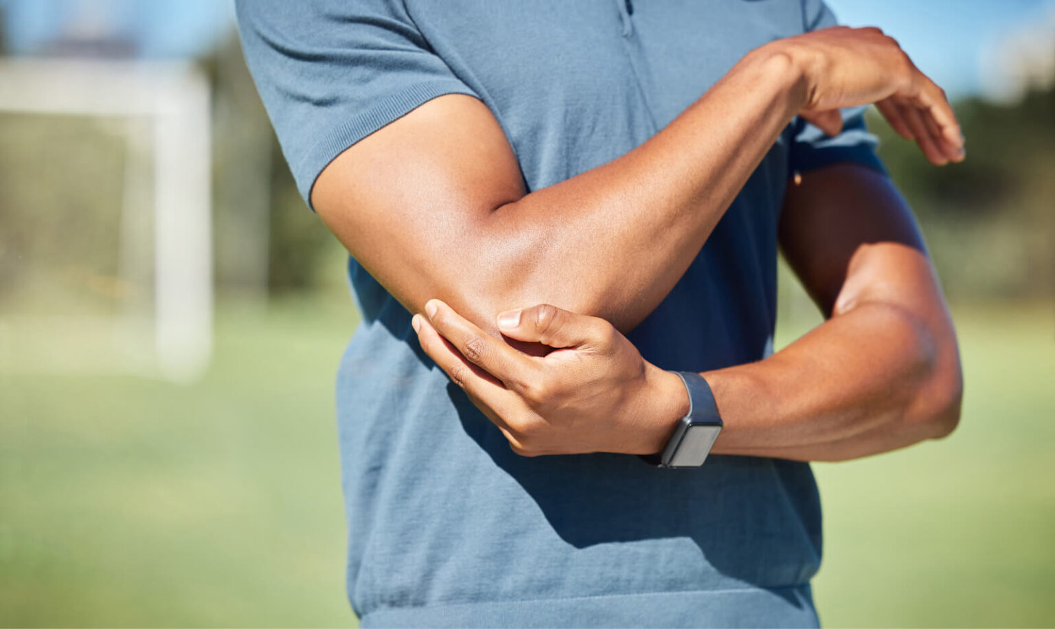 Man holding elbow outdoors, representing joint pain potentially linked to low testosterone levels and treatment options at Gameday Men’s Health.