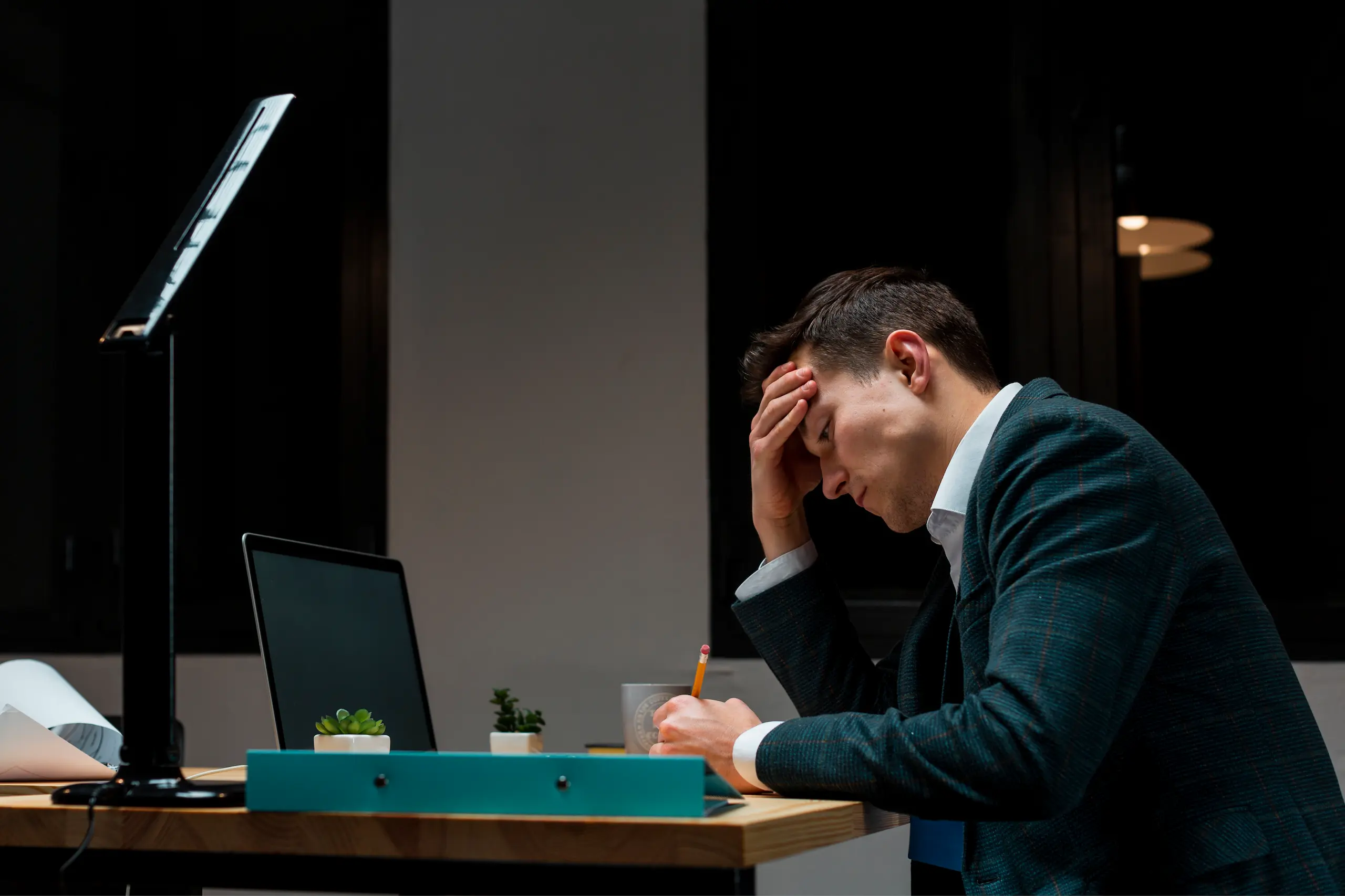 Stressed businessman working late at night with head in hand, symbolizing the impact of hypertension (high blood pressure) and whether or not taking testosterone is right for him.