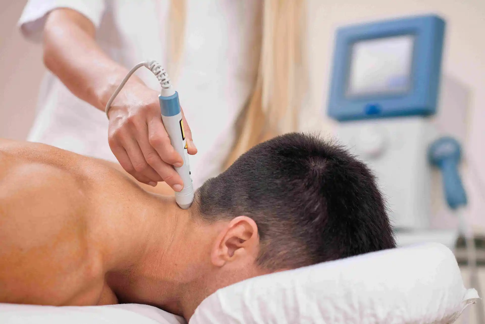 Medical professional applying shockwave therapy device to a patient’s neck during a non-invasive treatment session in a clinic.
