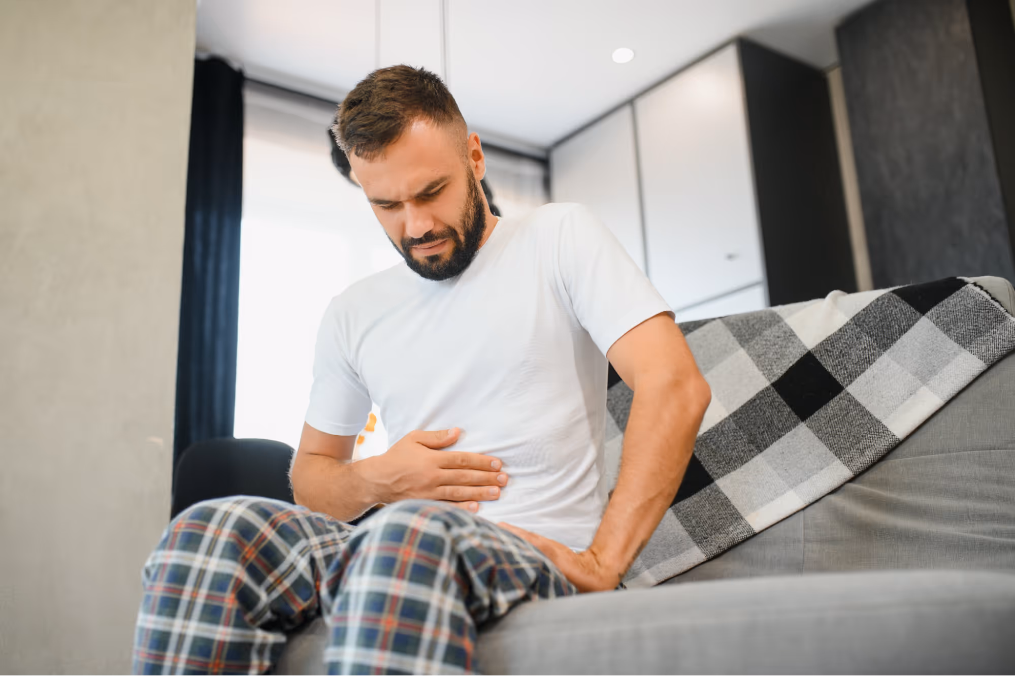 Man experiencing stomach discomfort at home, illustrating the connection between gut health and testosterone levels