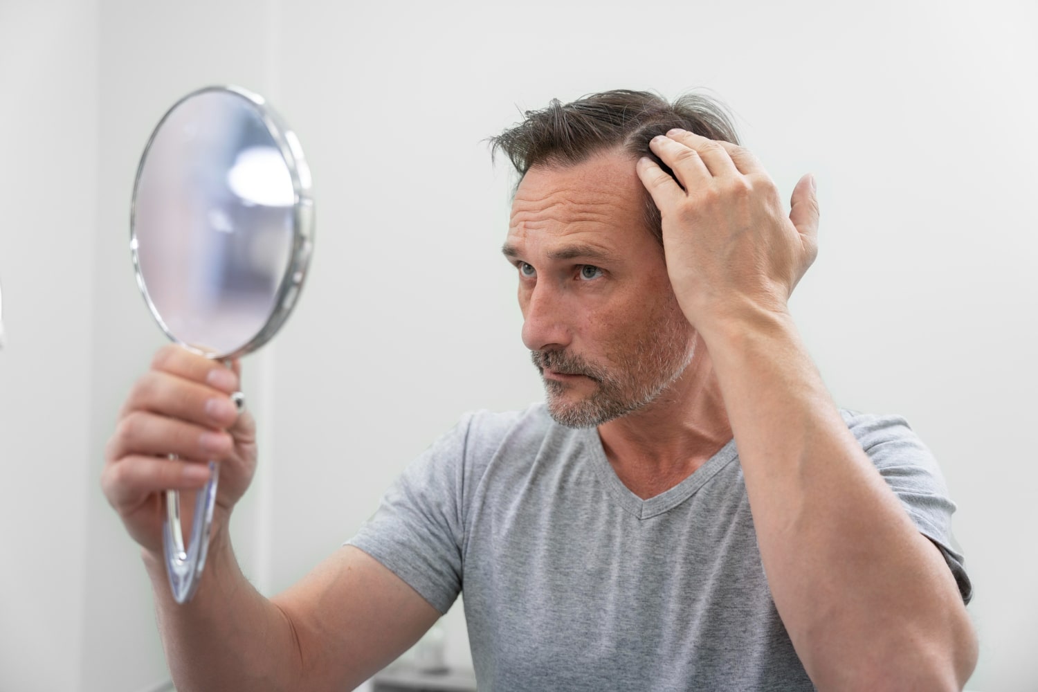 Man looking in the mirror, reflecting concerns about hair loss potentially linked to low testosterone levels.