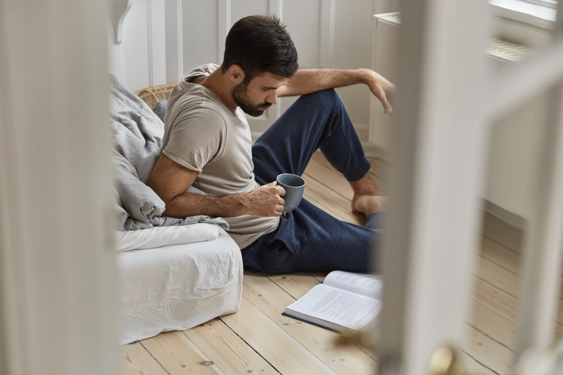 Thoughtful man reading while seated on the floor, reflecting proactive steps toward erectile dysfunction prevention.