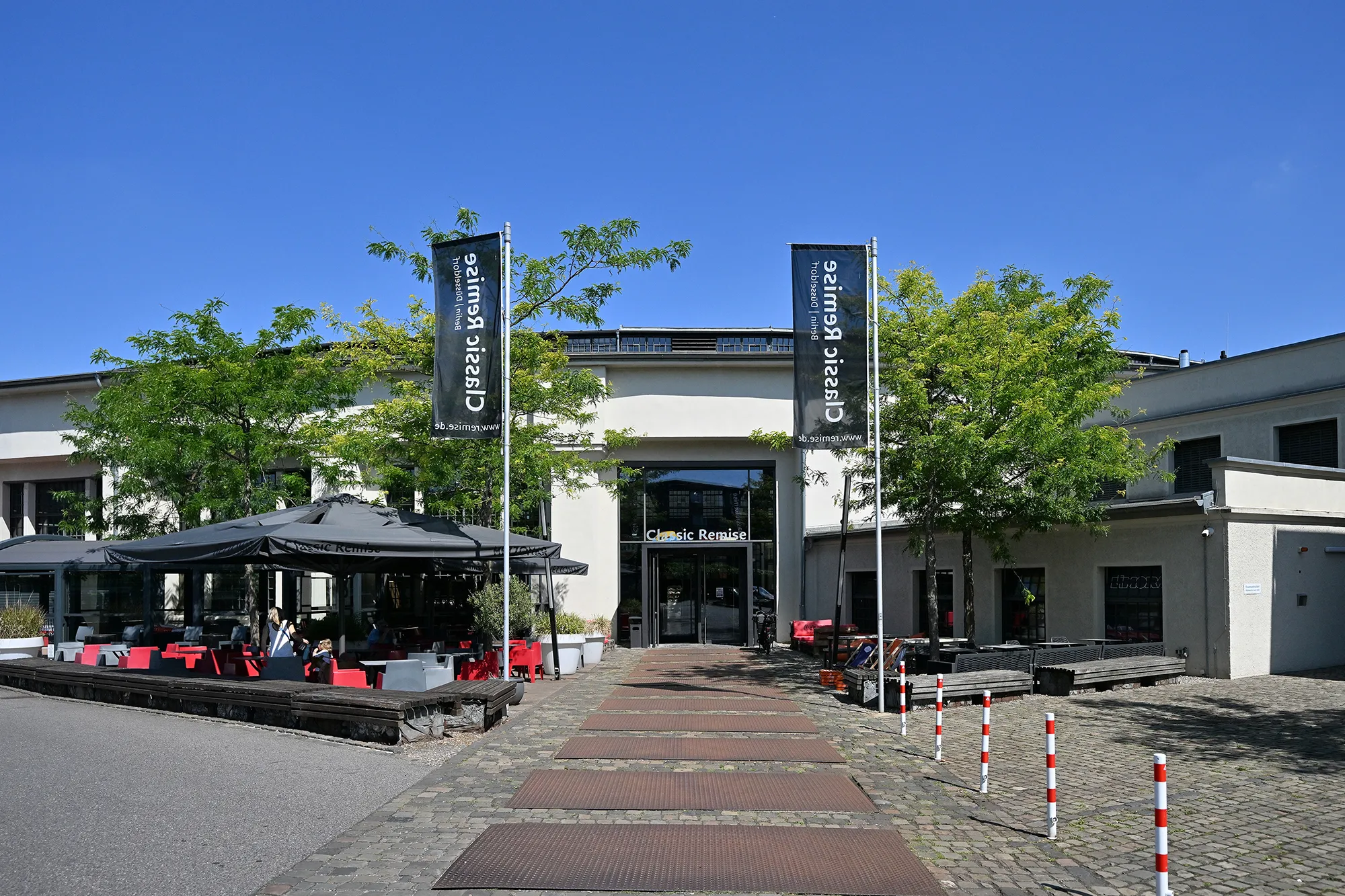 Haupteingang, der Classic Remise mit zwei Fahnen und einem gepflasterten Weg.