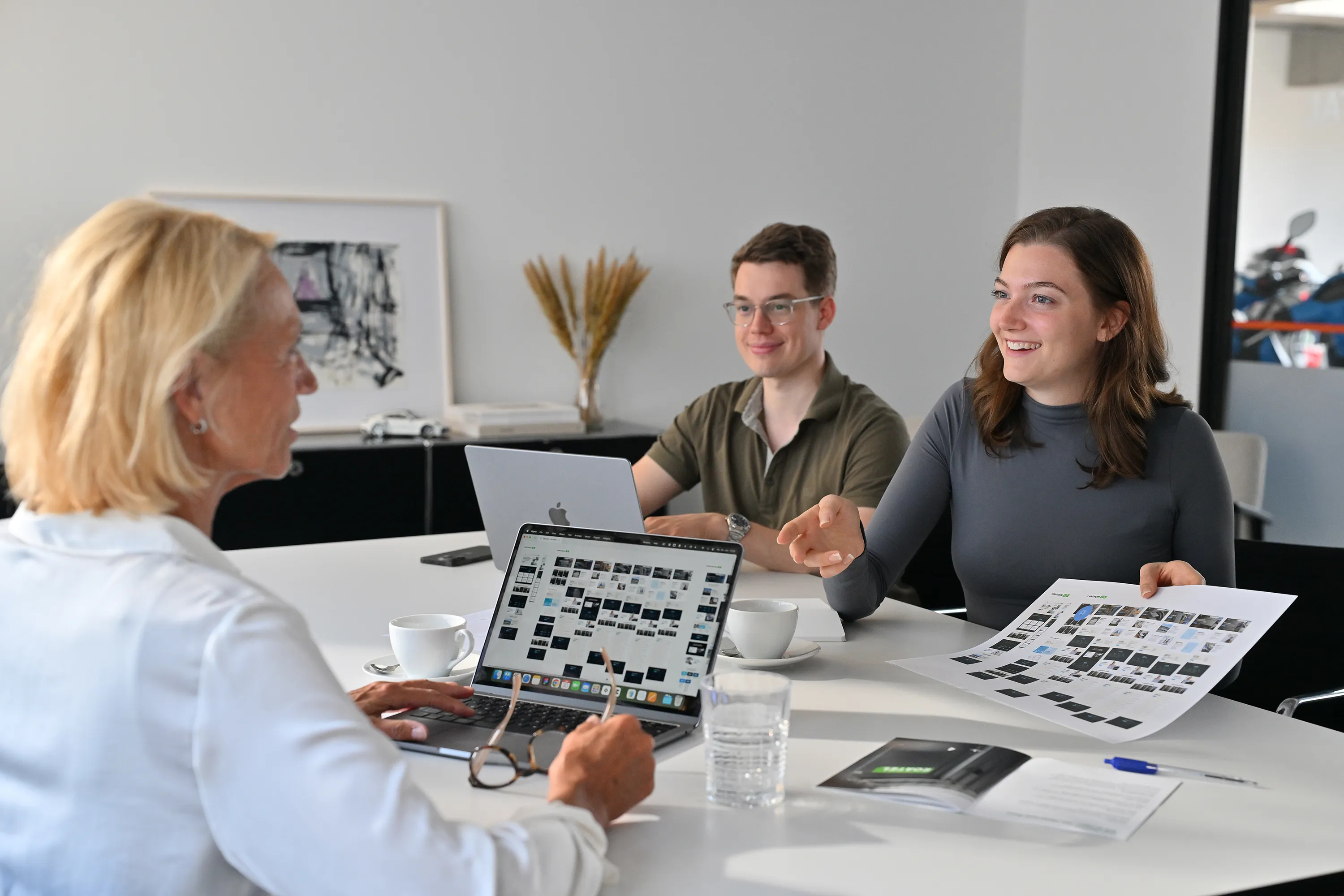 Drei Personen sitzen am Schreibtisch und unterhalten sich.