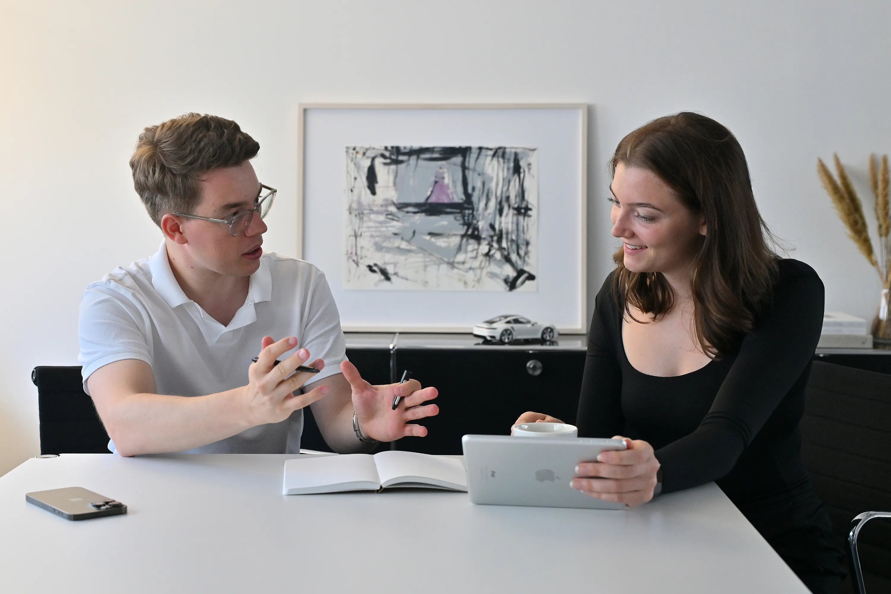 Zwei Personen sitzen am Schreibtisch und sprechen miteinander.