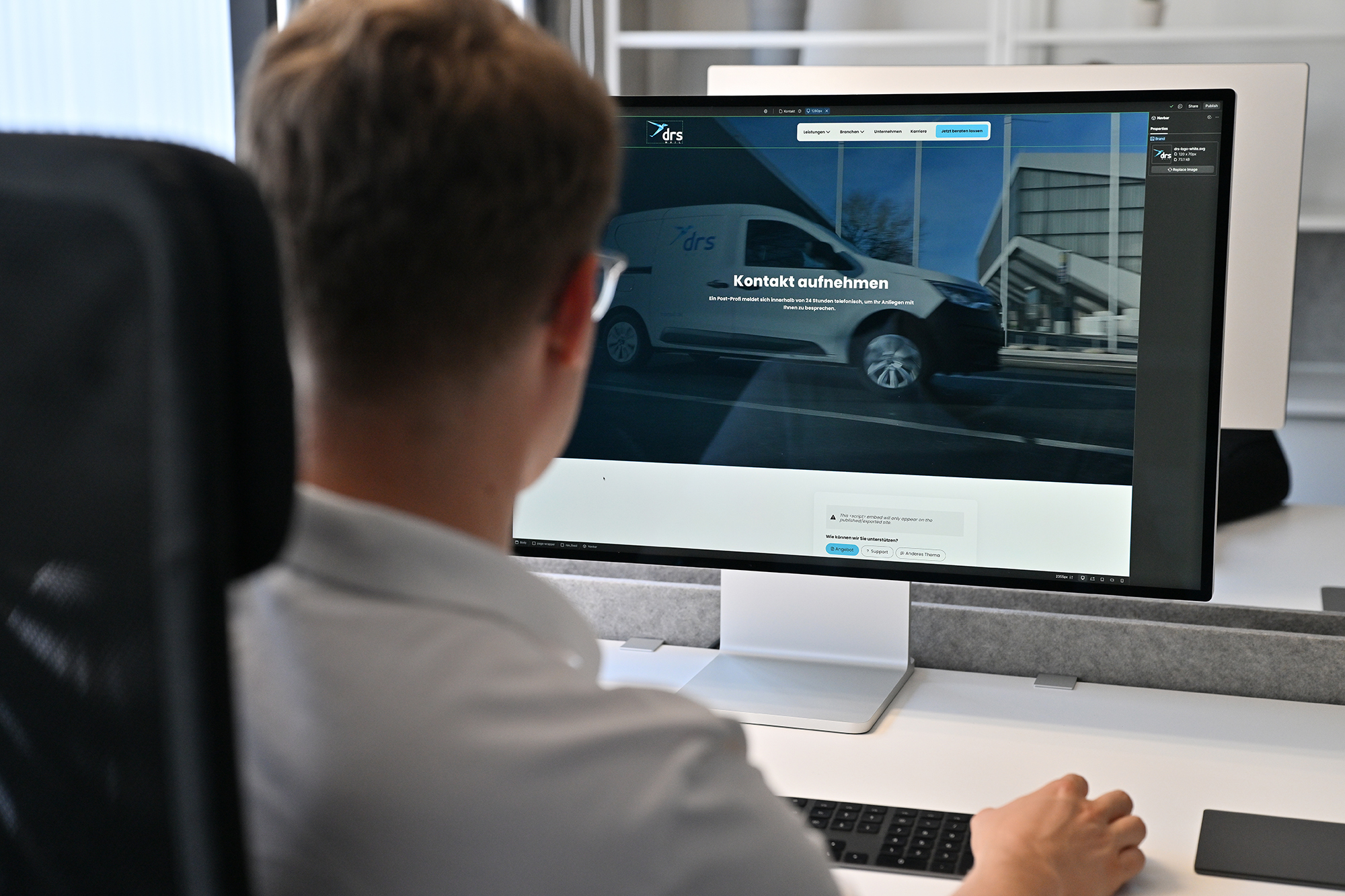 Person sitzt am Schreibtisch und schaut auf einen Monitor mit einer Website, die einen Lieferwagen und die Überschrift ‚Kontakt aufnehmen‘ zeigt.