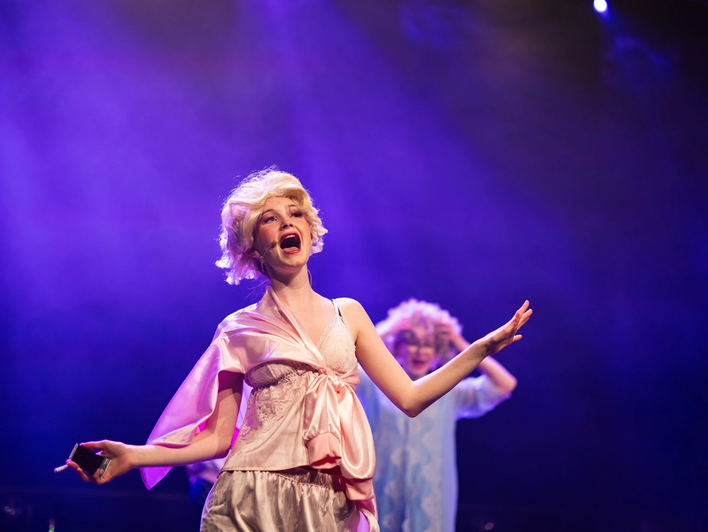 En elev på scenen under en teaterforestilling med dramatisk lyssetting i lilla toner, et bilde som fanger uttrykk, kreativitet og sceneglede ved Ringerike Folkehøgskole.