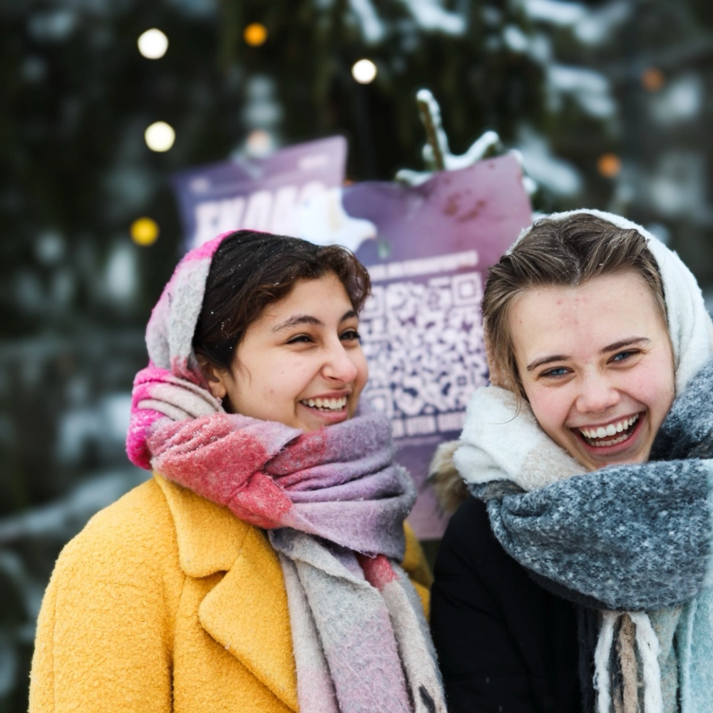 To elever fra Ringerike Folkehøgskole ler sammen ute i snøen, et bilde som viser vennskap, vinterglede og folkehøgskolemiljø.