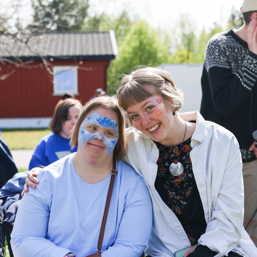To elever fra Ringerike Folkehøgskole smiler med ansiktsmaling under arrangement ute på skolens område, et bilde som viser glede, kreativitet og inkludering.