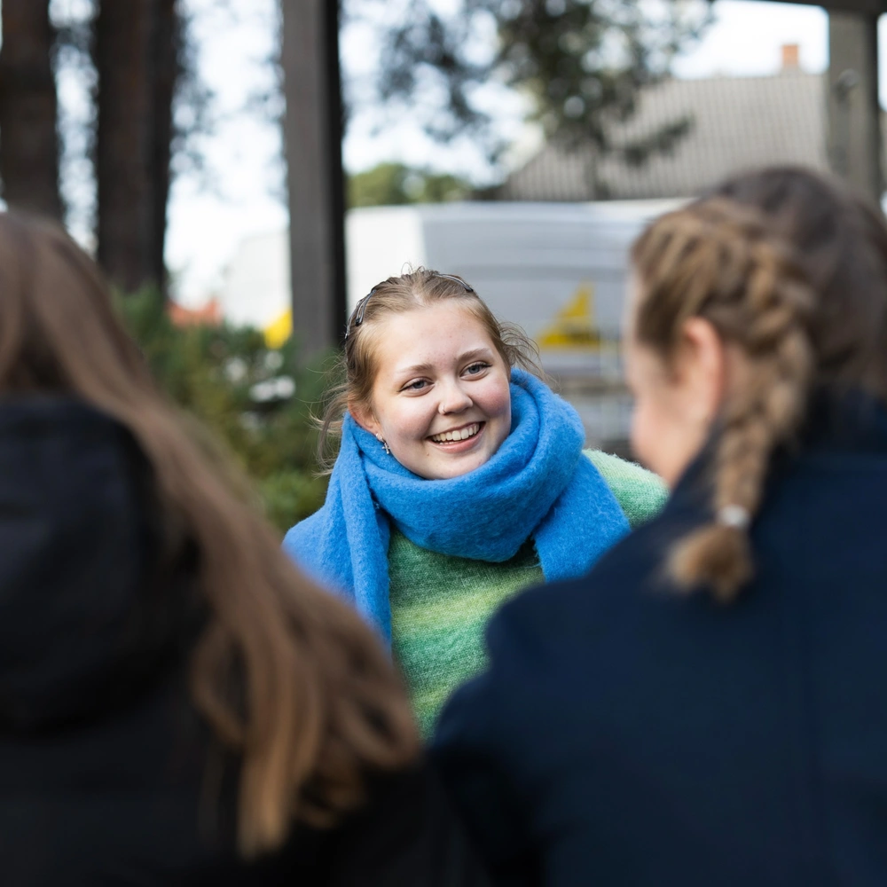Elev fra Ringerike Folkehøgskole smiler og prater med medelever ute, et bilde som viser vennskap, trygghet og sosialt fellesskap.