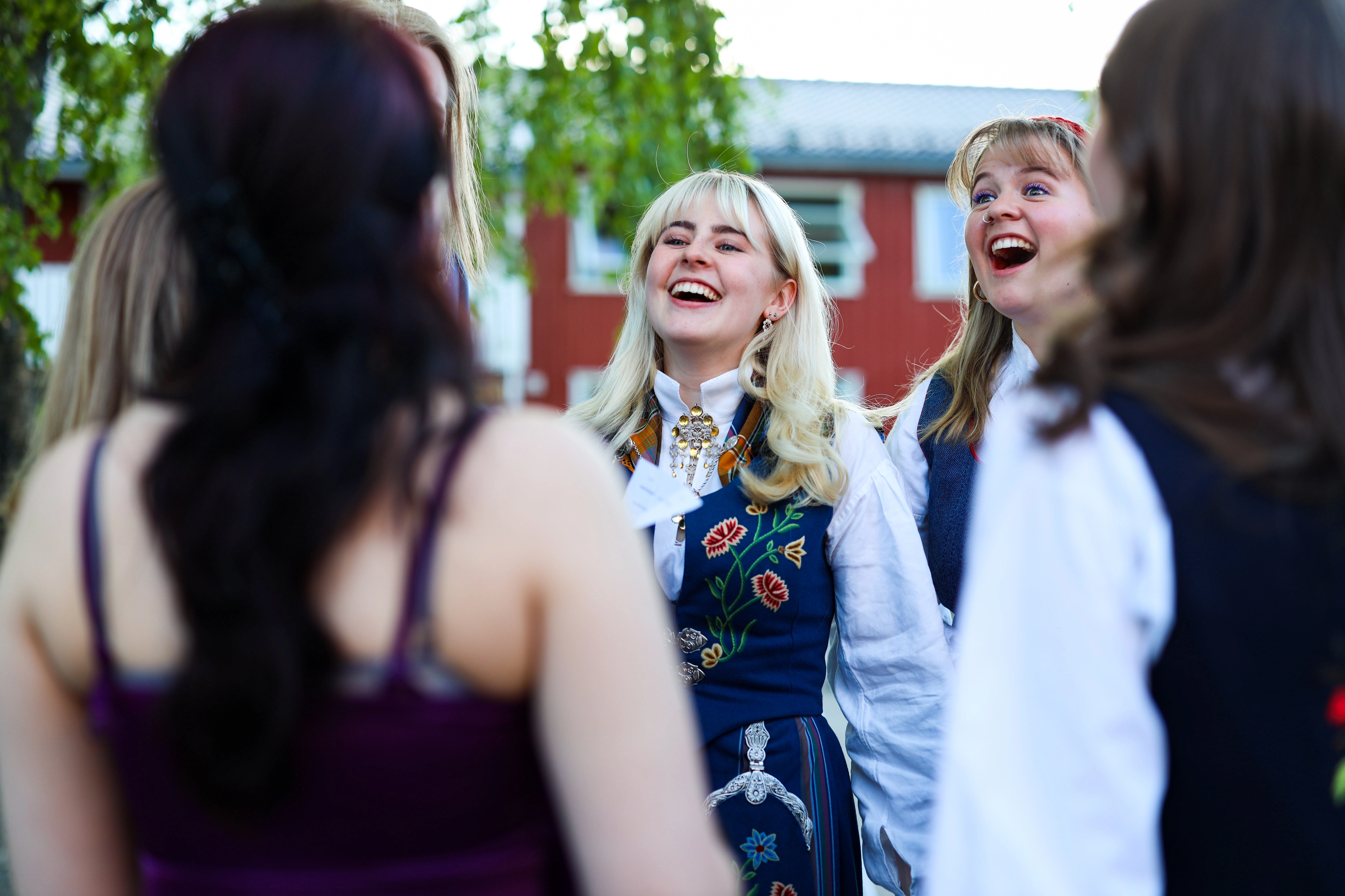 Elever ved Ringerike Folkehøgskole feirer i bunad og ler sammen ute, et bilde som viser samhold, tradisjon og glede ved skolens avslutning.