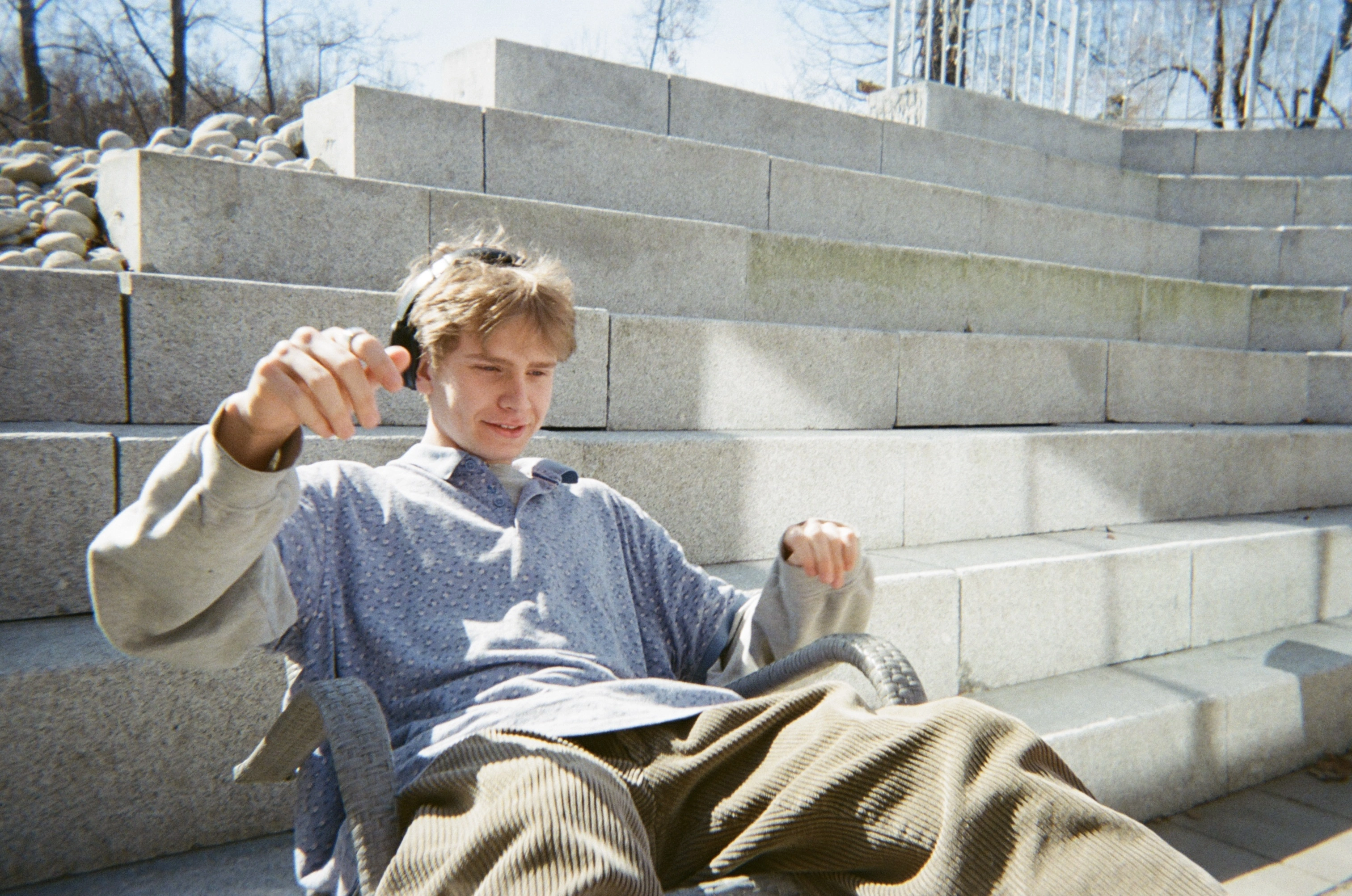 Elev fra linjen Visual arts på Ringerike Folkehøgskole slapper av ute i sola med hodetelefoner, et uttrykk for hverdagsliv på skolen.