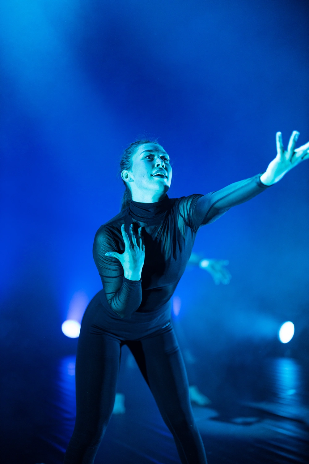 Elev fra Ringerike Folkehøgskole opptrer på scenen i en moderne danseforestilling med blått scenelys.