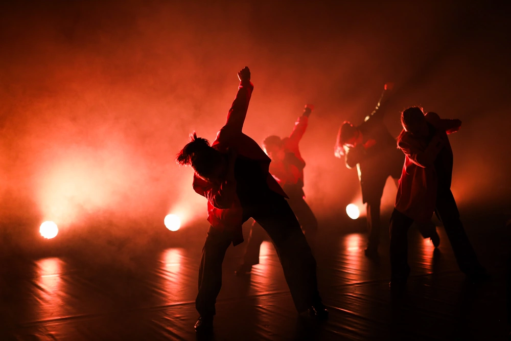 Elever fra Ringerike Folkehøgskole danser på scenen i dramatisk lyssetting, som del av skolens dans- og scenekunstlinje.