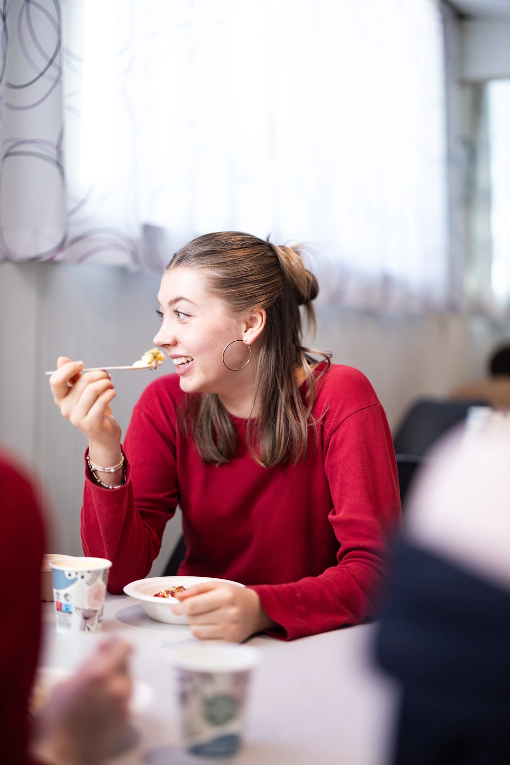 Elev ved Ringerike Folkehøgskole spiser frokost og smiler sammen med medelever i skolens trivelige matsal.
