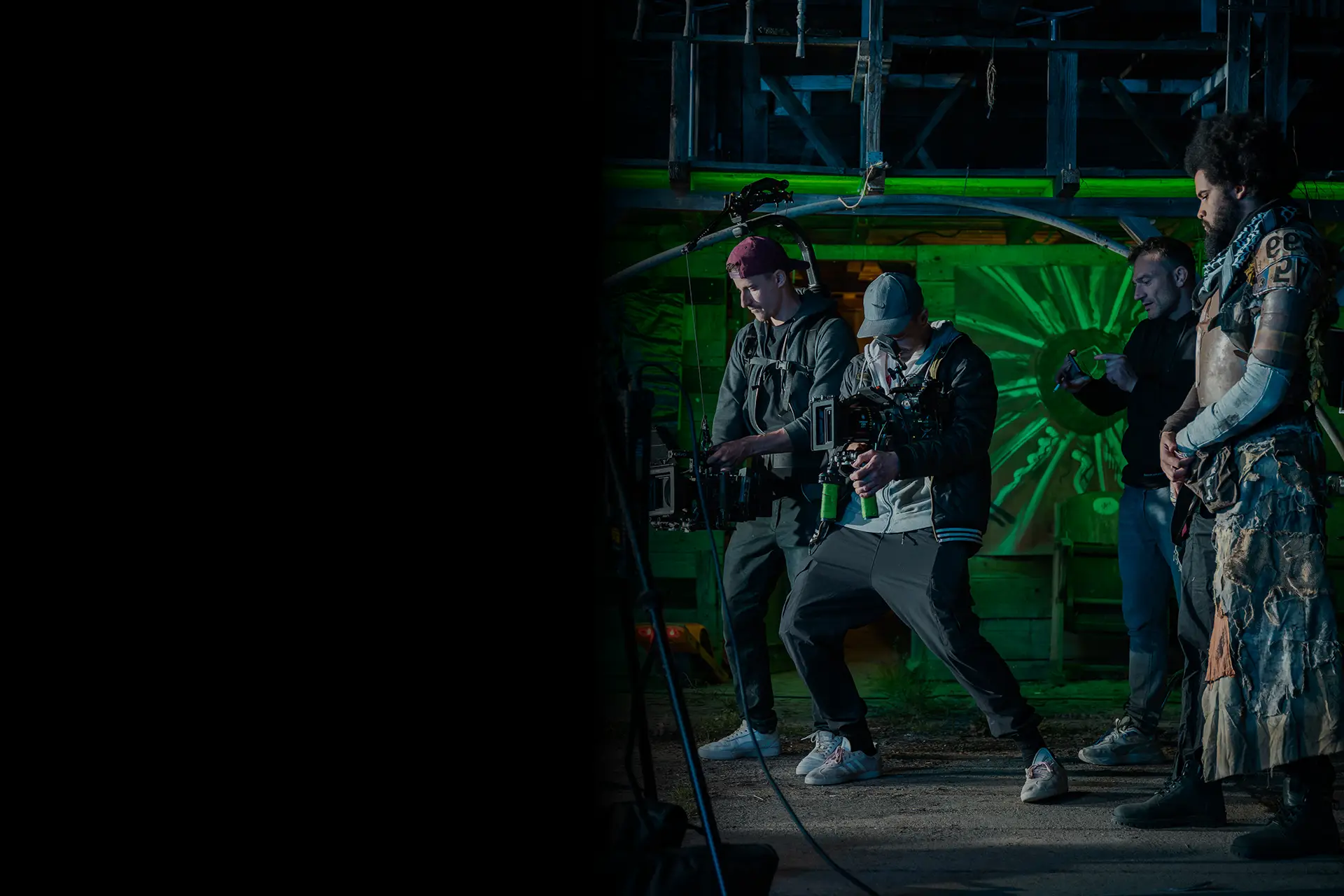 Man operating a professional video camera indoors with a focused expression and backlighting behind him.