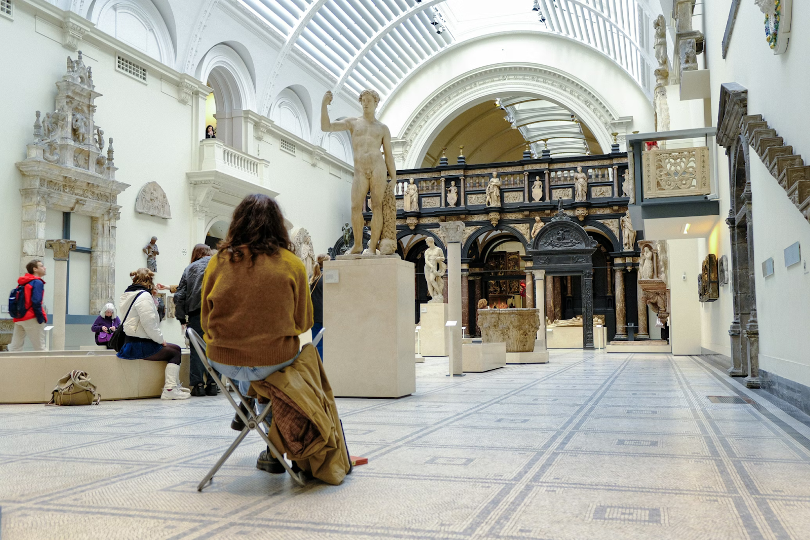 Woman sitting-down and resting in front of a sculpture at the Victoria and Albert Museum in Kensington, London