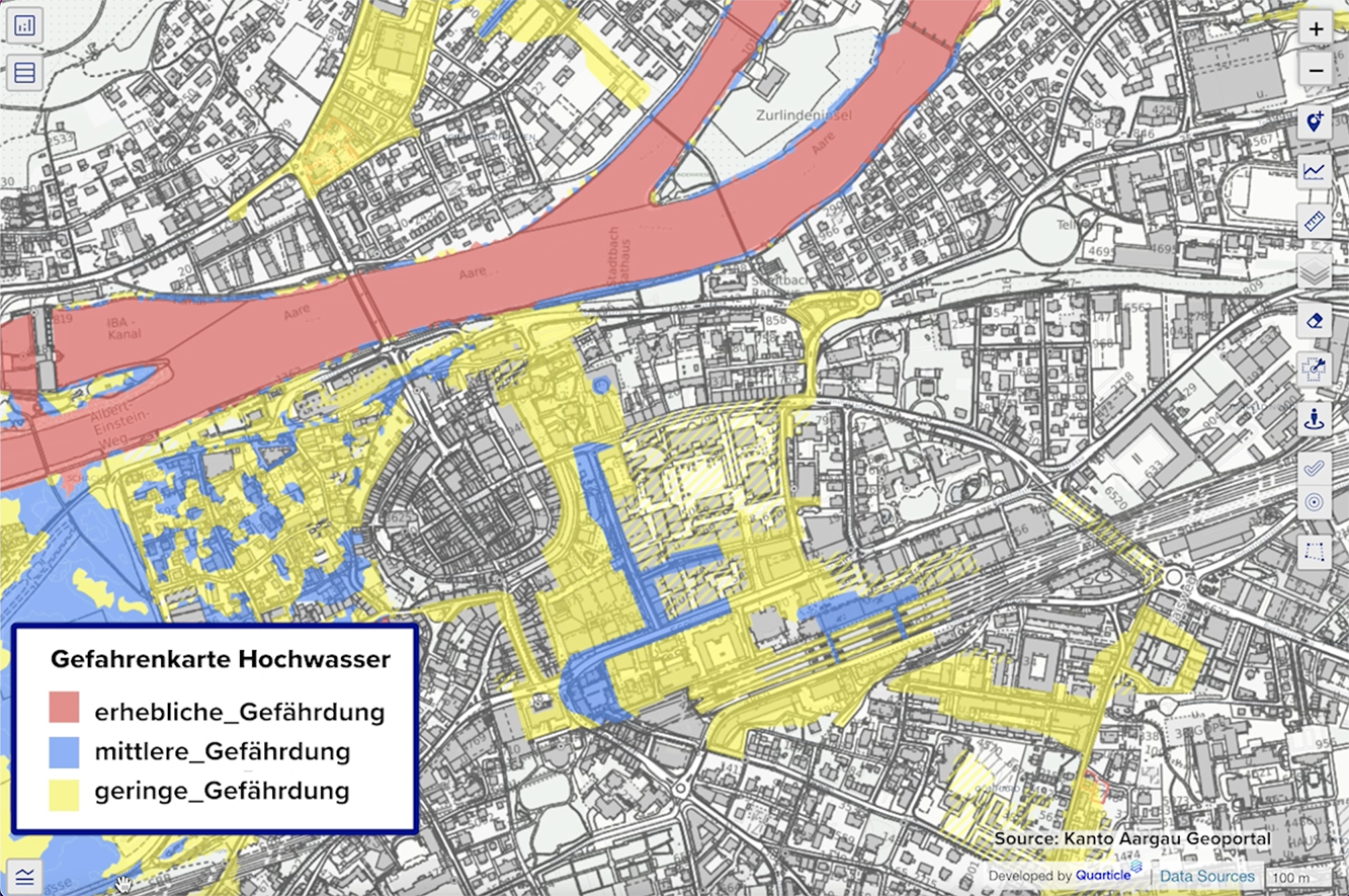 Graph by Quarticle geospatial intelligence app displays a detailed map of Aargau Canton, featuring a grey buildings layer overlaid with a flood hazard layer. The flood risk is color-coded: red areas indicate significant risk, blue areas highlight moderate risk, and yellow areas represent low risk. A legend titled "Gefahrenkarte Hochwasser" explains the risk categories, and the interactive map tools are visible on the right.