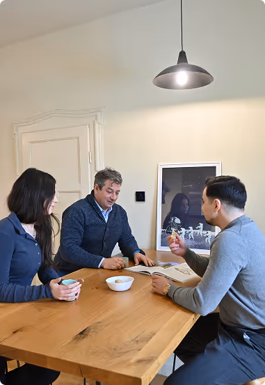 Three individuals engaged in a collaborative discussion around a wooden table in a bright office setting.