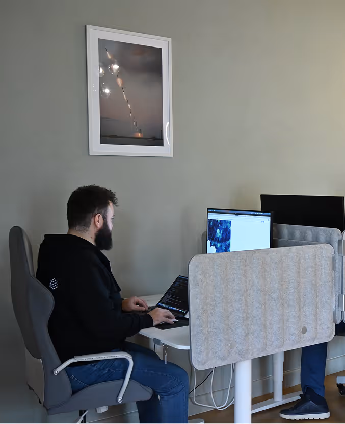 A professional looking at a monitor and sitting at a desk in a modern office environment.