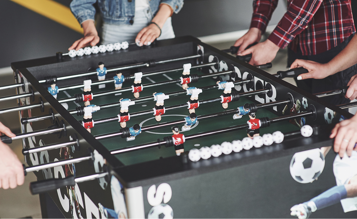 Four people playing a game of foosball in an office area.