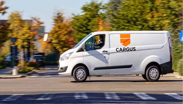 A white Cargus delivery van driving on a sunlit road. The image is connected to the out-of-home network optimization performed by Quarticle for Cargus. 