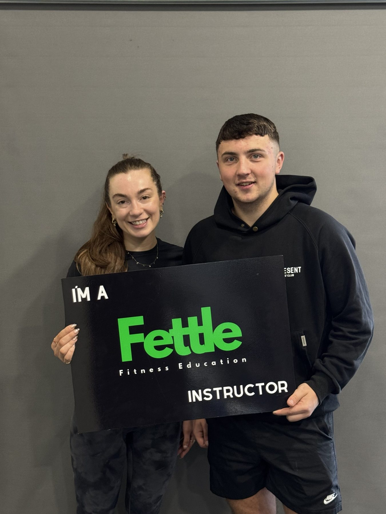 Two Fettle graduates holding an I'm a Fettle Instructor sign