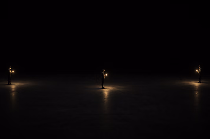 Three identical figures holding glowing light sources stand evenly spaced in a dark, empty space with faint illuminated areas around each figure.