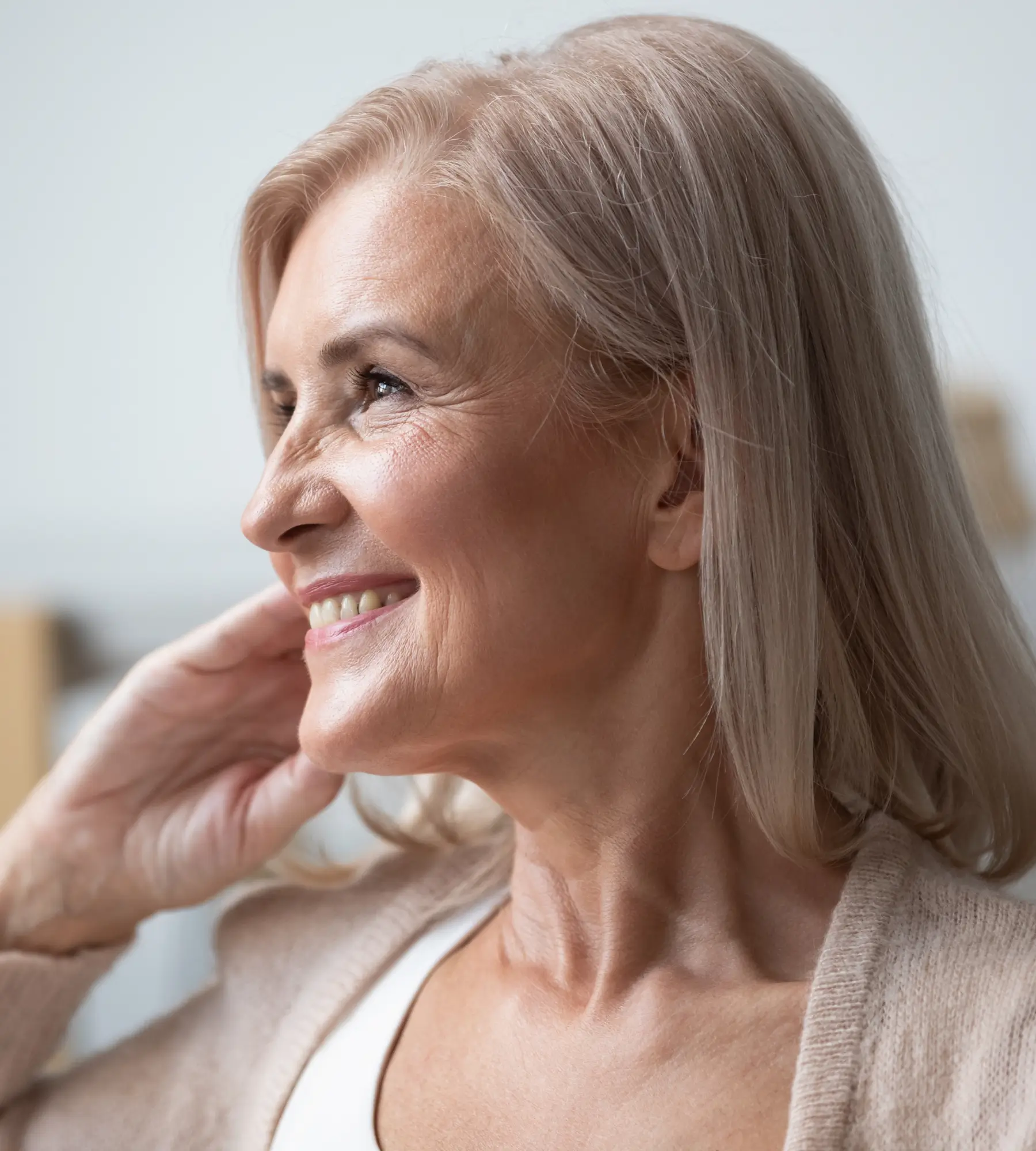 Smiling woman with long, light hair looking to the side, wearing a beige sweater.