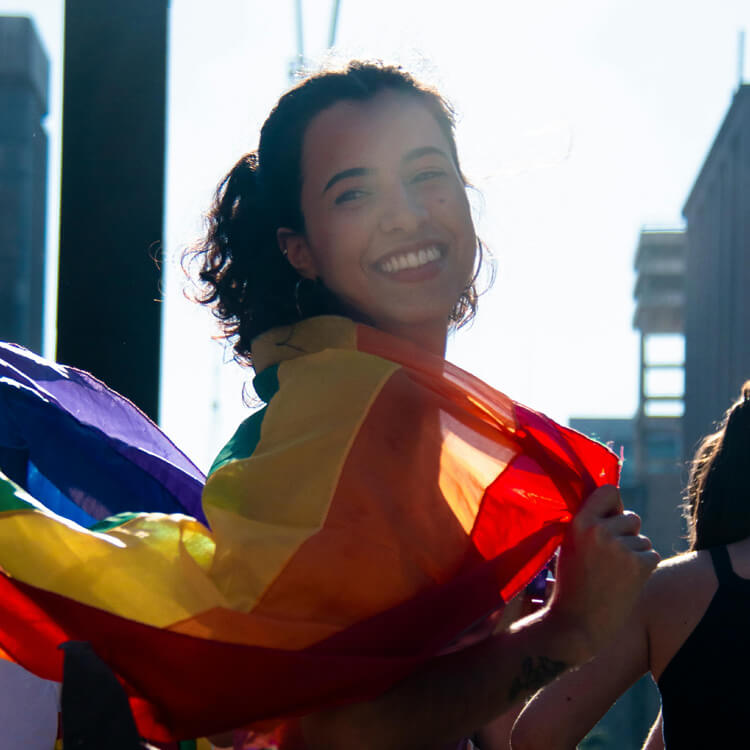 Une jeune femme marche dans la rue avec un drapeau arc-en-ciel au vent