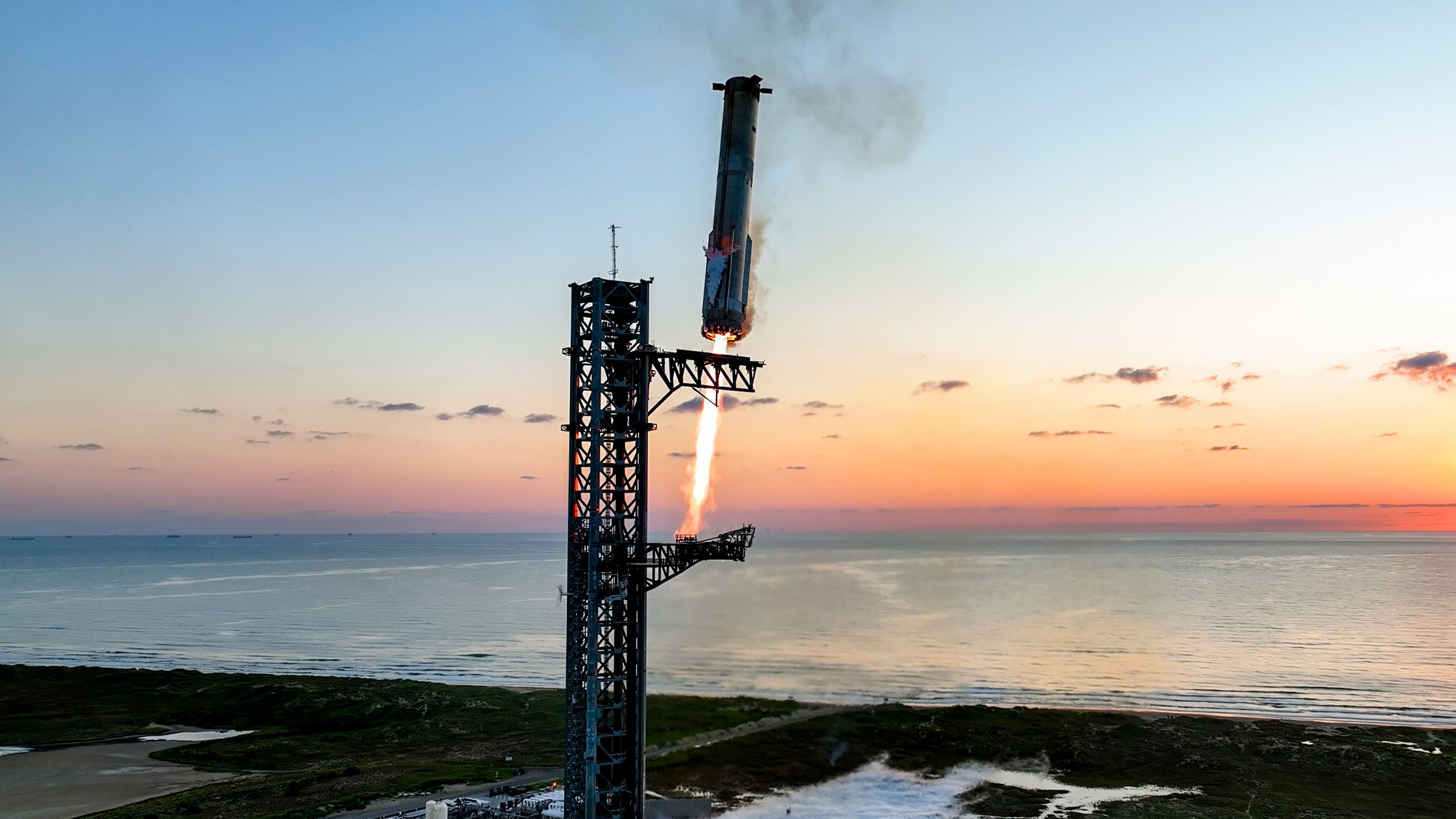 Rocket booster landing vertically on a platform over the ocean at sunset.
