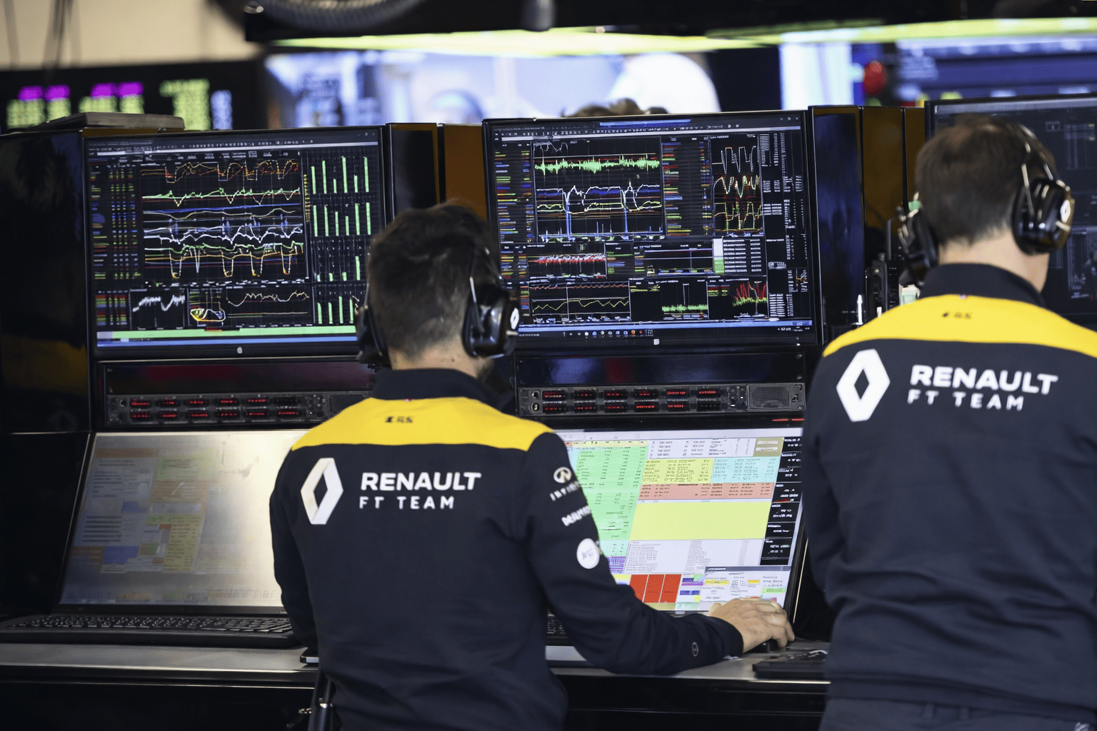 Two Renault F1 Team engineers working at a telemetry station with multiple screens showing racing data and analytics.