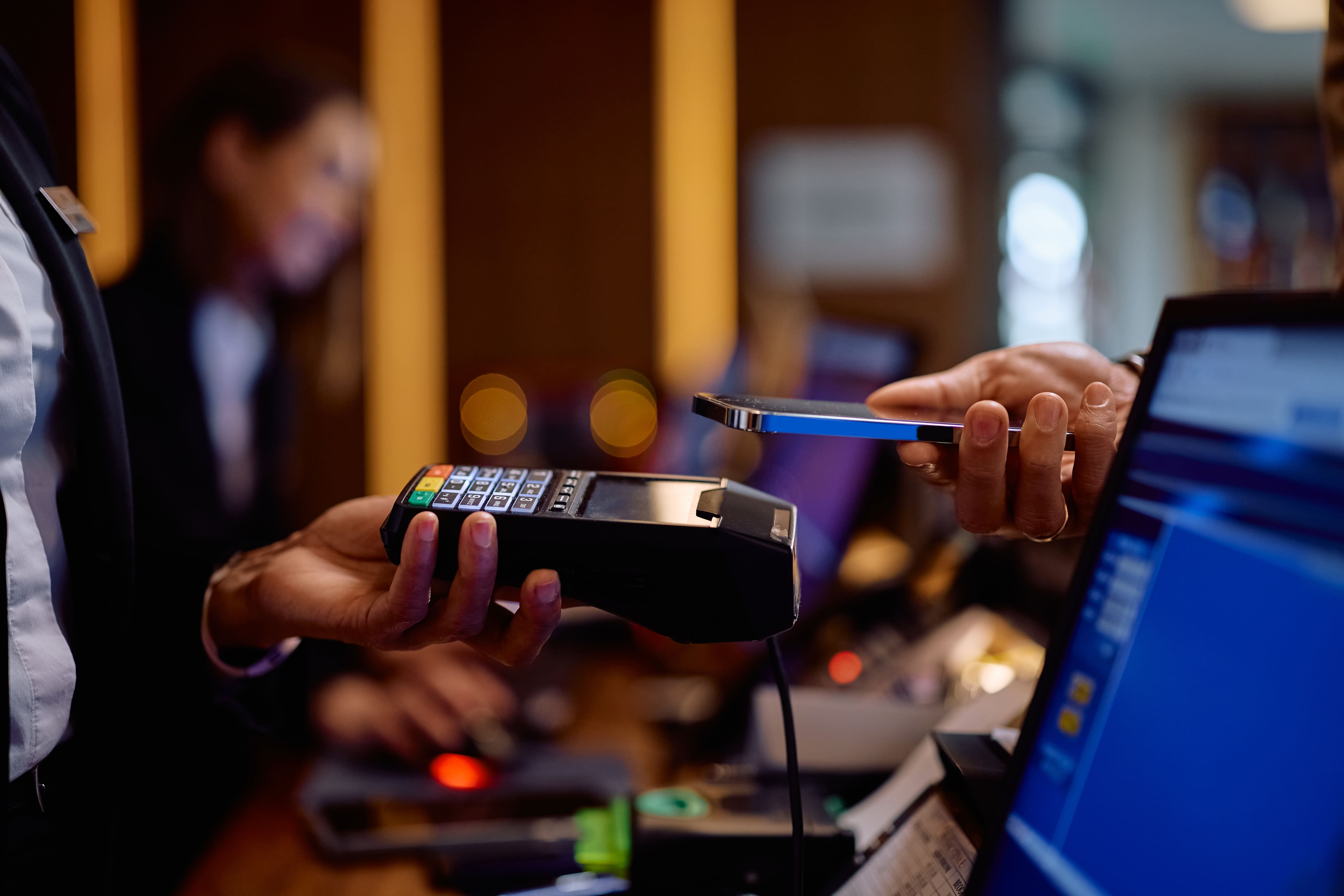Person holding a payment terminal while another person makes a contactless payment with a smartphone.