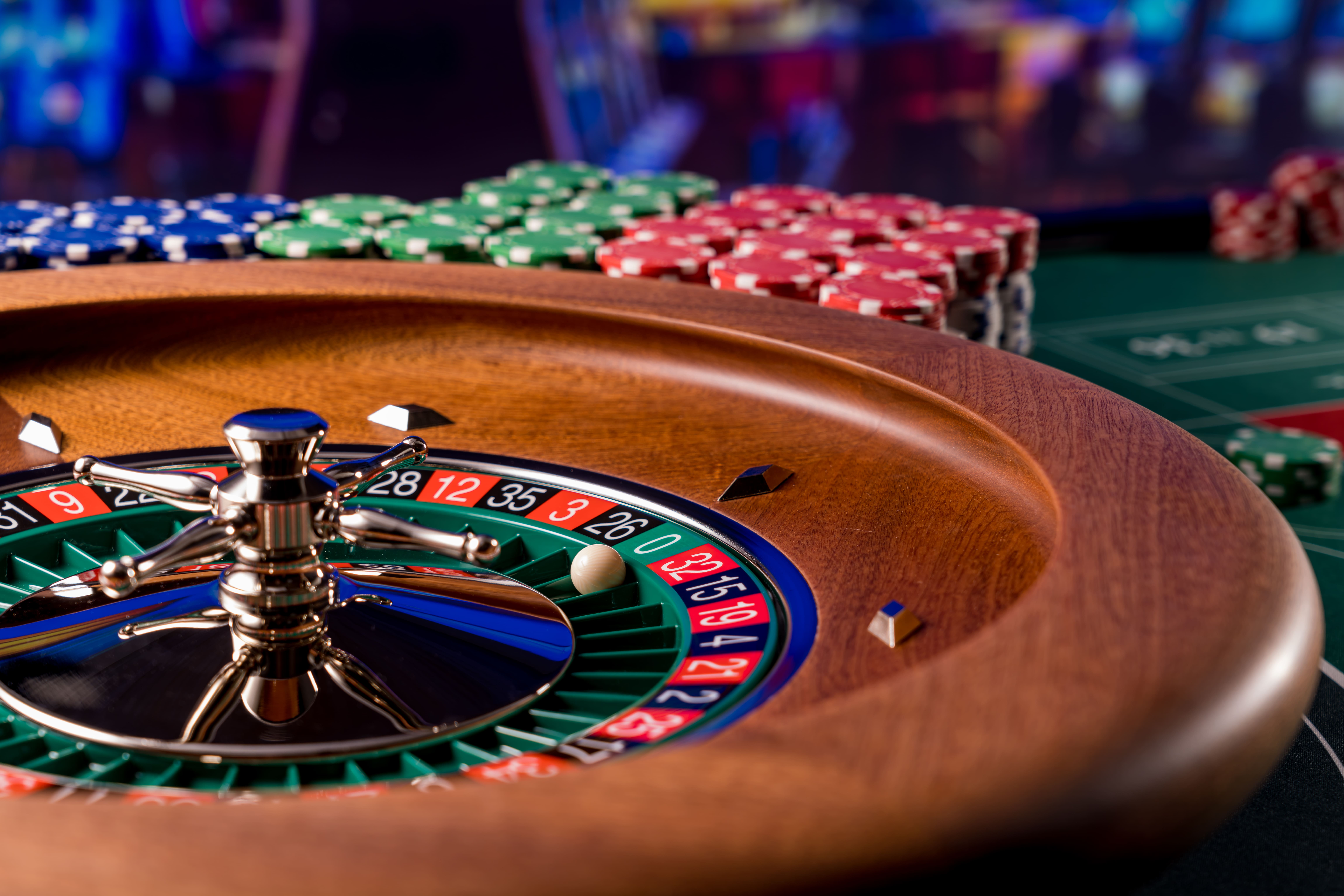 Close-up of a roulette wheel with a white ball near number 4 and stacks of colorful poker chips in the background.