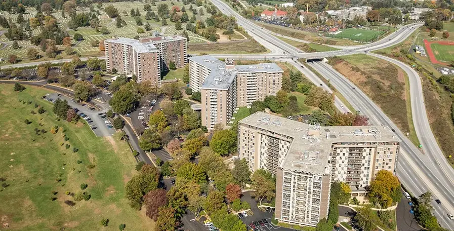Aerial of apartment buildings with trees and parking lots.